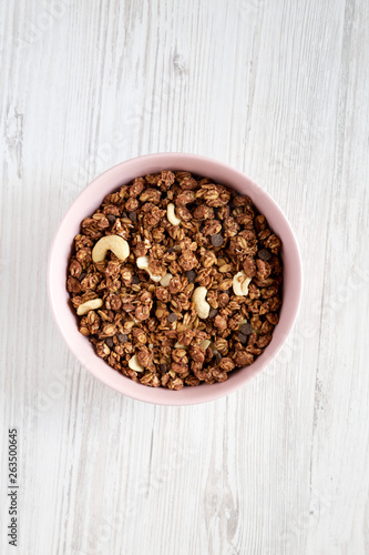 Homemade chocolate granola with nuts in a pink bowl over white wooden background, top view. From above, overhead, flat lay.