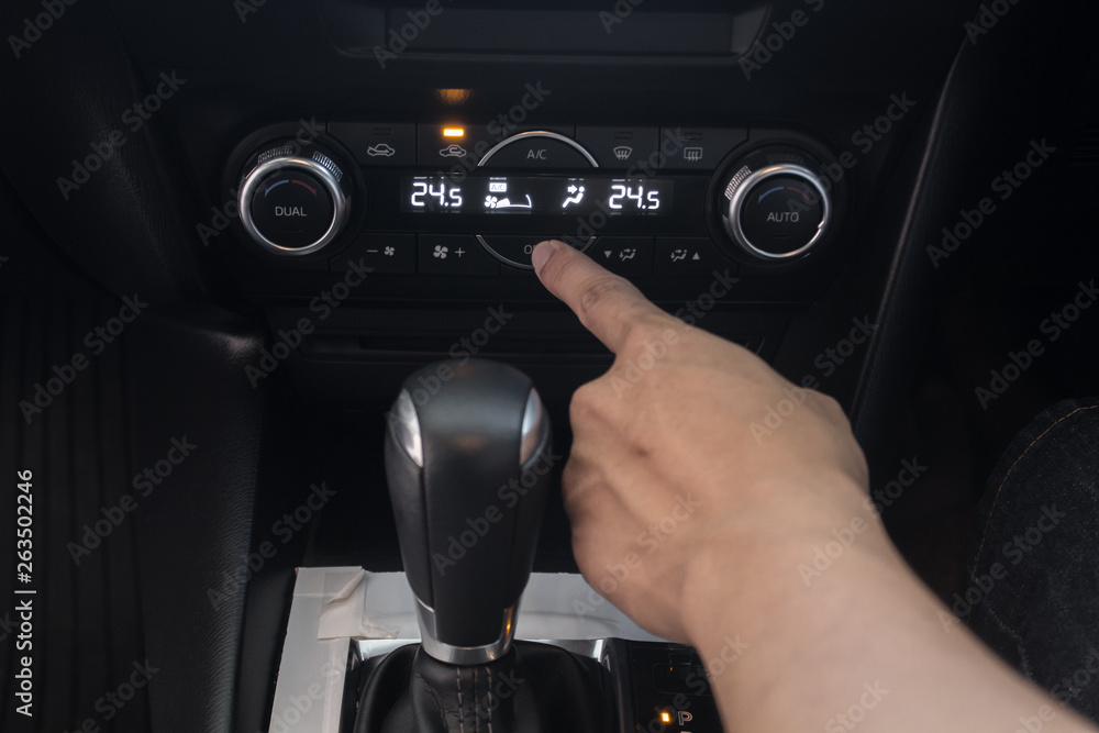 hand on air control buttons of a modern car.