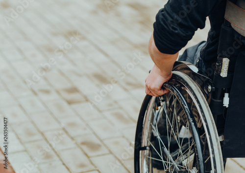 Close-up of male hand on wheel of wheelchair during walk in park photo