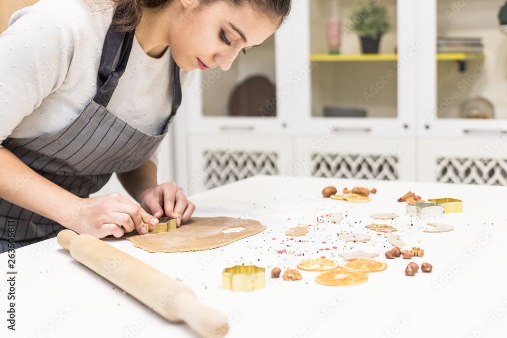 Young pretty woman prepares the dough and bakes gingerbread and cookies in the kitchen. She makes a star shape on the dough. Merry Christmas and Happy New Year. Young pretty woman prepares the dough and bakes gingerbread and cookies in the kitchen. She makes a star shape on the dough. Merry Christmas and Happy New Year.