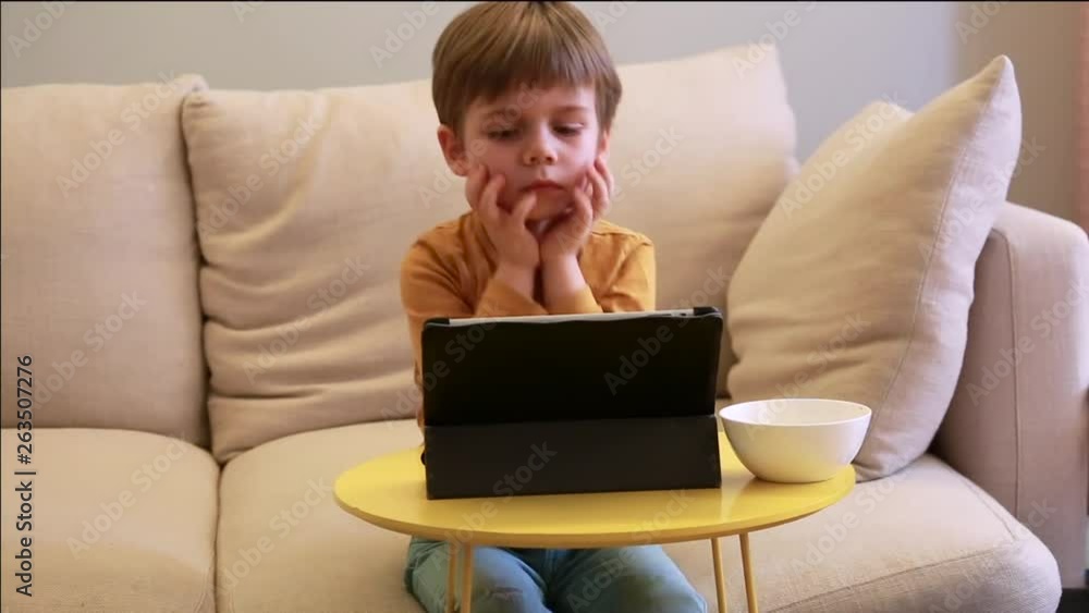 Child using tablet pc on bed at home. Cute boy on sofa is watching cartoon, playing games and learning from laptop. Education, fun, leisure, happiness, modern computer technology and communication. Child using tablet pc on bed at home. Cute boy on sofa is watching cartoon, playing games and learning from laptop. Education, fun, leisure, happiness, modern computer technology and communication.