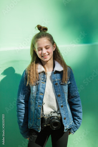 Cute twelve year old girl with camera stands near the green wall.. photo