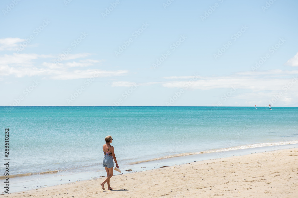 older woman walking on a empty beautiful beach 