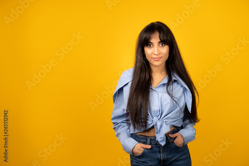 Young beautiful girl in a blue shirt posing for a photo on a yellow background.