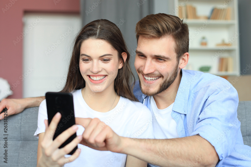 Young couple watching online content in a smart phone sitting on a sofa at home in the living room. Young couple watching online content in a smart phone sitting on a sofa at home in the living room.