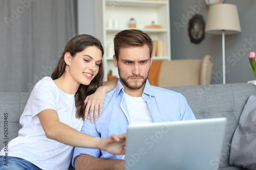 Young couple doing some online shopping at home, using a laptop on the sofa.