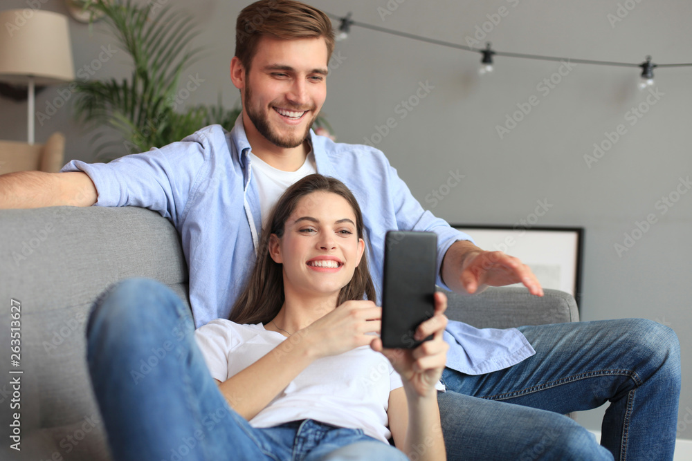 Young couple watching online content in a smart phone sitting on a sofa at home in the living room. Young couple watching online content in a smart phone sitting on a sofa at home in the living room.