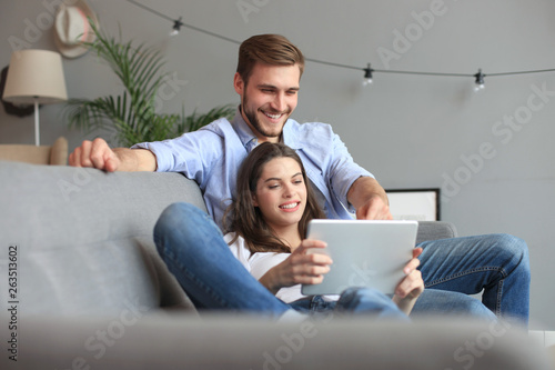 Young couple watching media content online in a tablet sitting on a sofa in the living room.