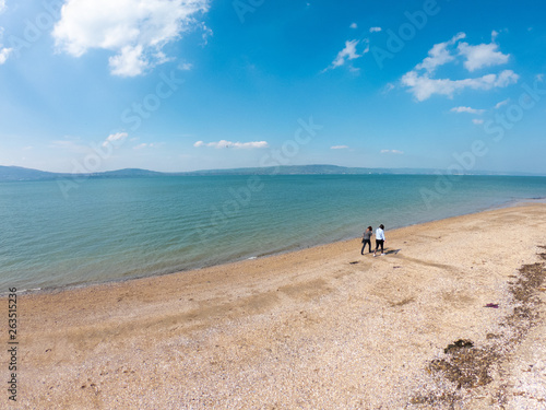 Back view of two women standing on beach and looks at sea against blue sky in Holywood, Northern Ireland, aerial view 