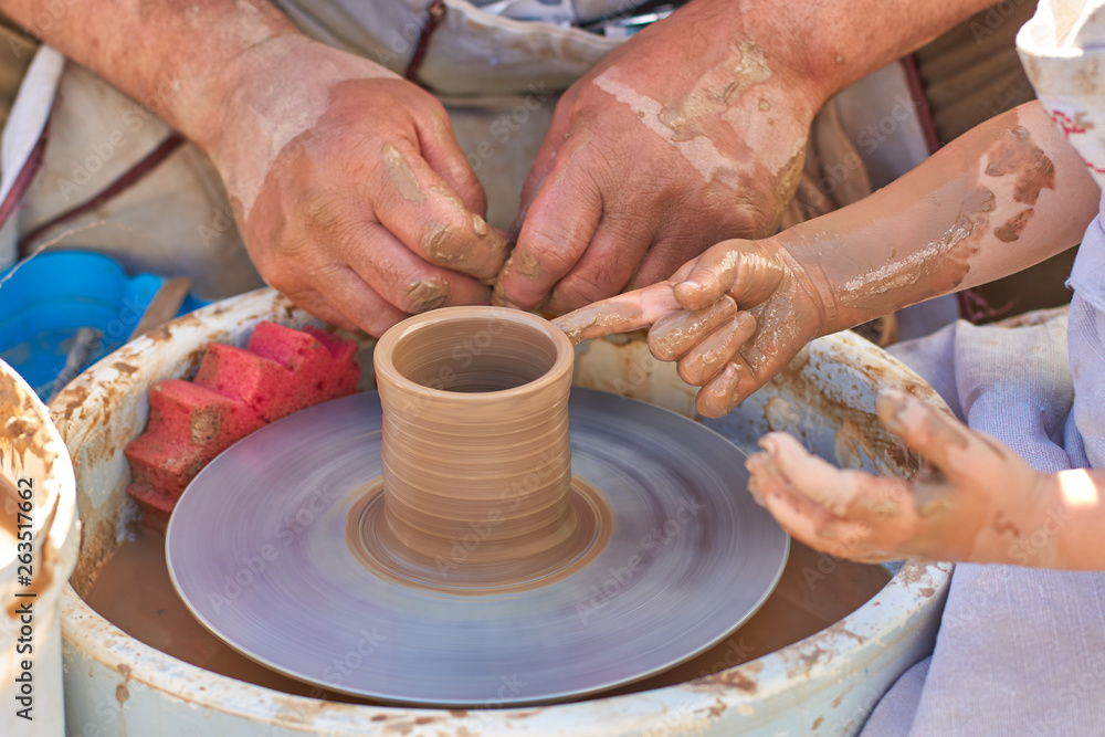 Training pottery, hands of a child and a master on clay, close-up