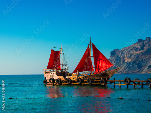 Old wooden ship with red sails on the pier