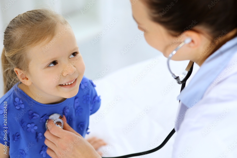 Doctor examining a little girl by stethoscope. Happy smiling child patient at usual medical inspection. Medicine and healthcare concepts Doctor examining a little girl by stethoscope. Happy smiling child patient at usual medical inspection. Medicine and healthcare concepts