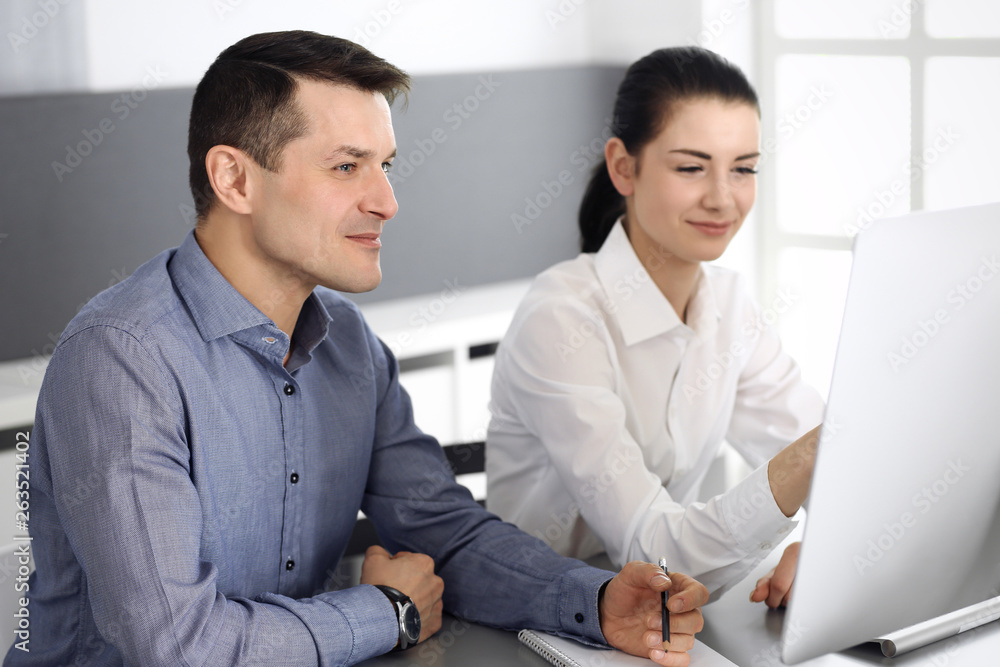Obraz premium Cheerful smiling businessman and woman working with computer in modern office. Headshot at meeting or workplace. Teamwork, partnership and business concept 