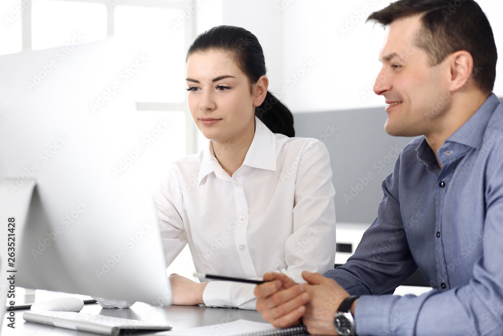 Cheerful smiling businessman and woman working with computer in modern office. Headshot at meeting or workplace. Teamwork, partnership and business concept Cheerful smiling businessman and woman working with computer in modern office. Headshot at meeting or workplace. Teamwork, partnership and business concept