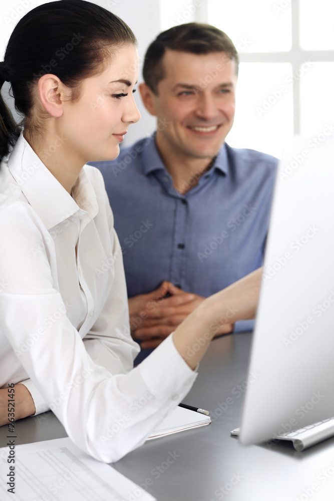 Cheerful smiling businessman and woman working with computer in modern office. Headshot at meeting or workplace. Teamwork, partnership and business concept Cheerful smiling businessman and woman working with computer in modern office. Headshot at meeting or workplace. Teamwork, partnership and business concept