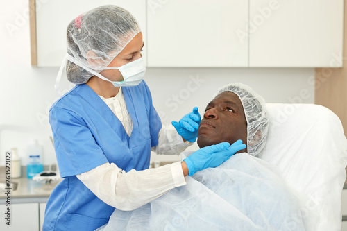 Cosmetician female examining patient face skin before aesthetic procedure
