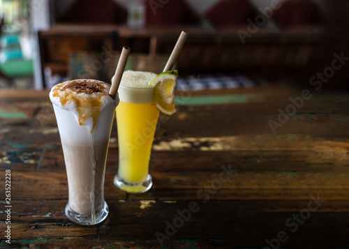 Freshly squeezed orange juice and chocolate milkshake in a tall glasses with a straw on a wooden vintage table in cafe. Copy space