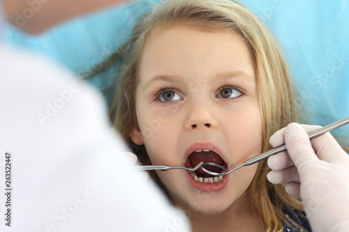 Little baby girl sitting at dental chair with open mouth and feeling fear during oral check up while doctor. Visiting dentist office. Medicine concept