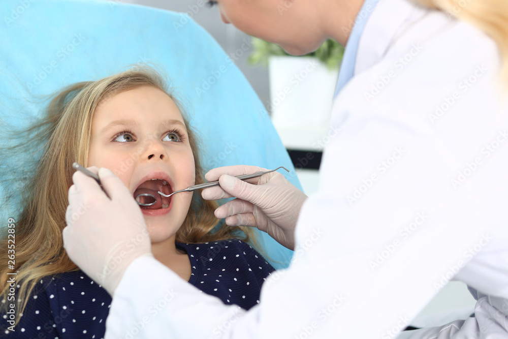 Little baby girl sitting at dental chair with open mouth and feeling fear during oral check up while doctor. Visiting dentist office. Medicine concept Little baby girl sitting at dental chair with open mouth and feeling fear during oral check up while doctor. Visiting dentist office. Medicine concept