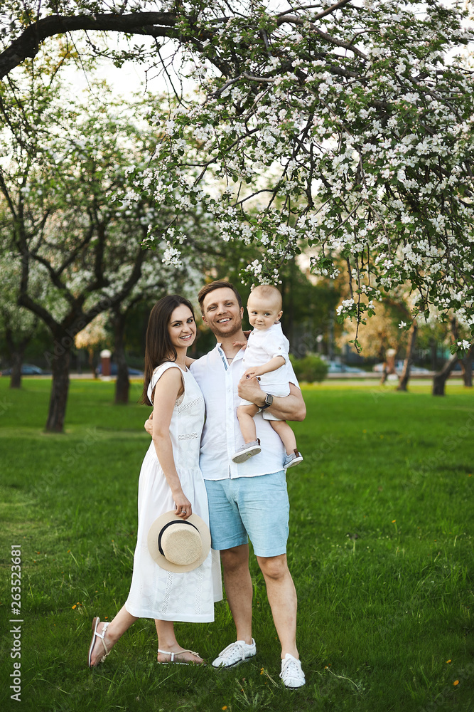 Beautiful young parents and their cute little son have fun near flowering trees, happy family Beautiful young parents and their cute little son have fun near flowering trees, happy family
