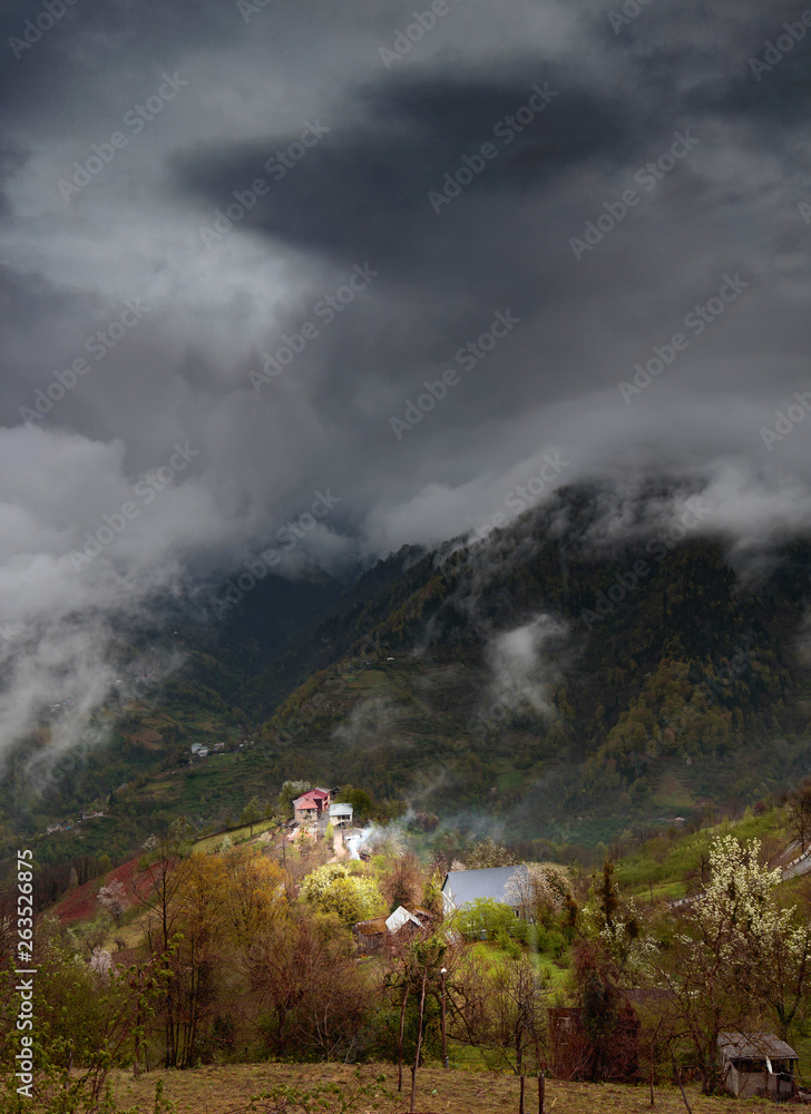 Caucasus village and mountains on dark moody day with big clouds.