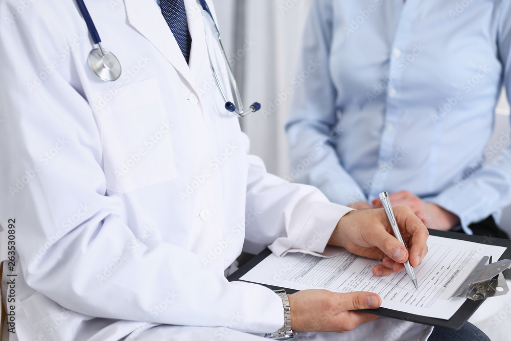 Male doctor holding application form while consulting female patient in hospital. Medicine and healthcare concept Male doctor holding application form while consulting female patient in hospital. Medicine and healthcare concept