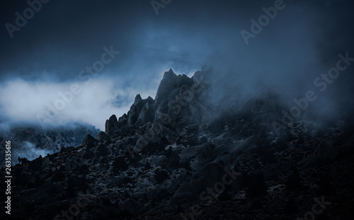Rocky mountain peaks surrounded by misty fog in the Sierra Nevada mountains near North Lake in Eastern California. The ominous foggy weather creats an emotional feel to the mist filled rugged scene