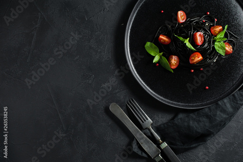 Black spaghetti with Basil and cherry tomatoes, vegetarian pasta. Black background, top view, space for text.