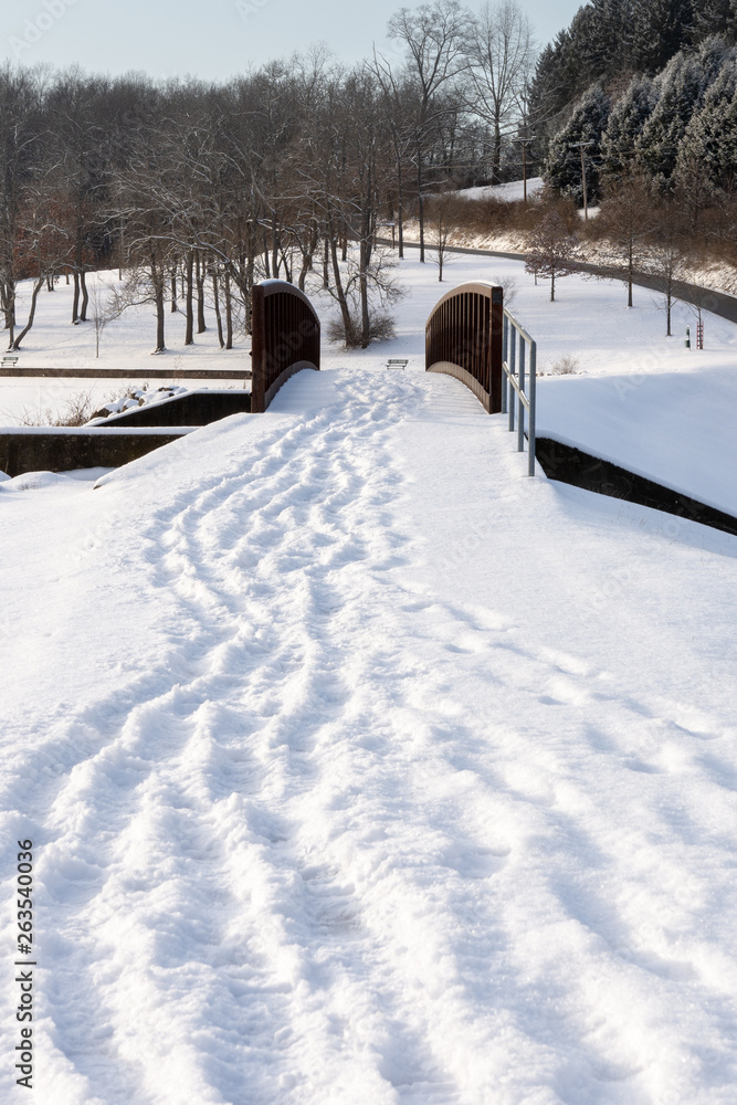 foot path covered in snow with many footprints of people leading and following over the snow covered bridge after a fresh snowfall