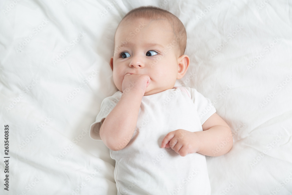Very scared little baby girl in white lying on a white bed. The baby teething Very scared little baby girl in white lying on a white bed. The baby teething