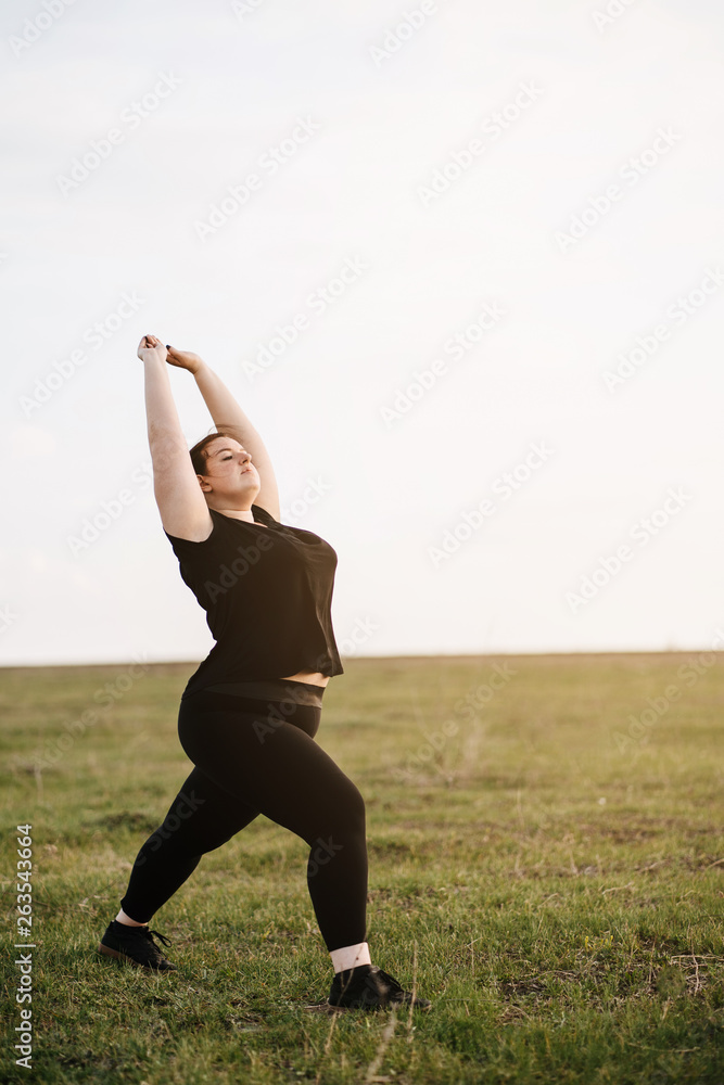 Young overweight woman doing morning yoga on the country road, open air activity. Healthy lifestyle, sport, weight loss Young overweight woman doing morning yoga on the country road, open air activity. Healthy lifestyle, sport, weight loss