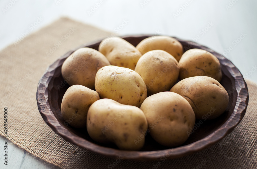 Raw potatoes in rustic wooden plate, on bright background. Organic agriculture & food concept. Raw potatoes in rustic wooden plate, on bright background. Organic agriculture & food concept.