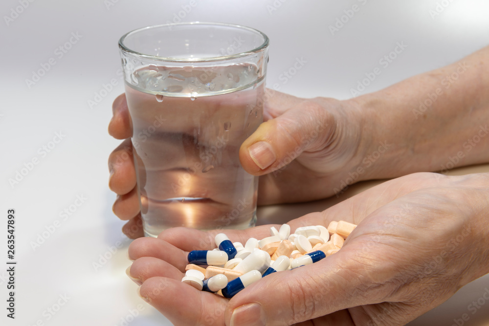 Una mano con farmacos y otra con un vaso de agua
