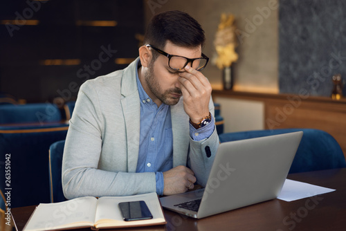 Mid adult businessman having headache while working on laptop in a cafe