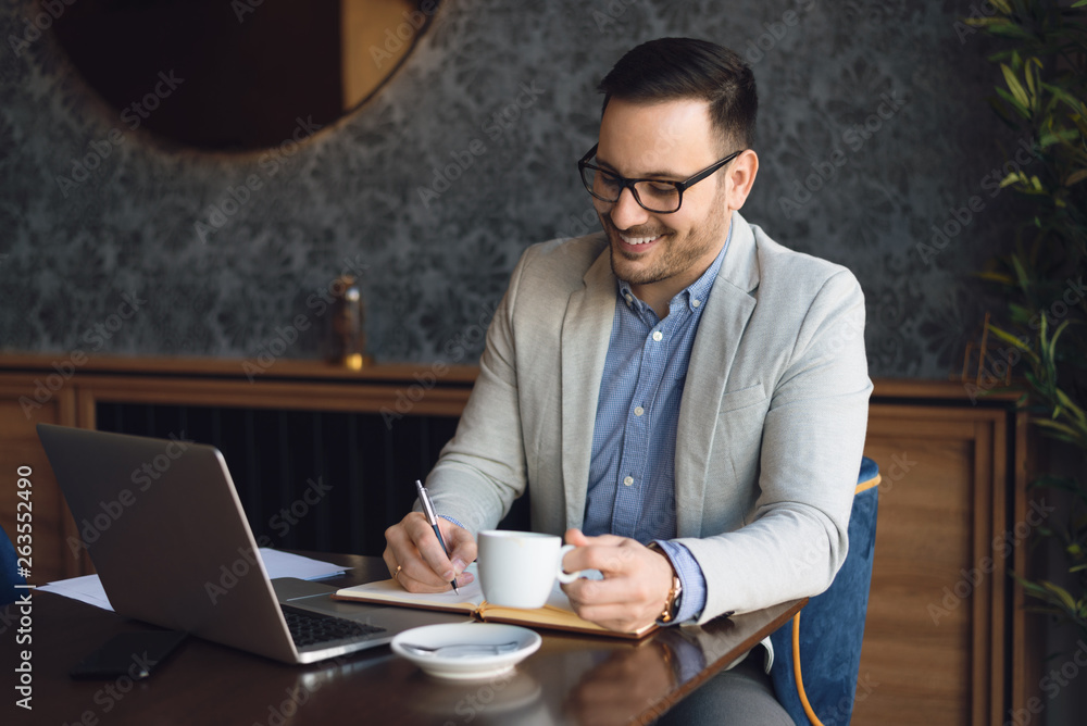 Young businessman writing something in a notebook and drinking coffee in a cafe. Young businessman writing something in a notebook and drinking coffee in a cafe.