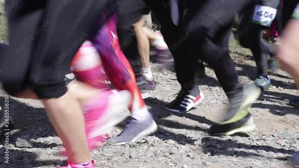 Crowd of amateur athletes running marathon cross country. Many human legs close up.
