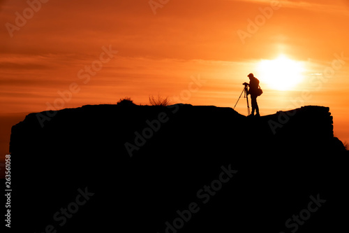 Silhouette of a photographer who shoots a sunset, on top of castle at sunset background.