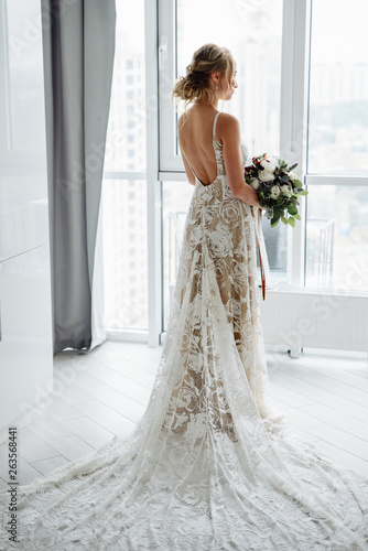 Fototapeta Gorgeous bride in a luxurious long dress with a bouquet in hand, stands and look