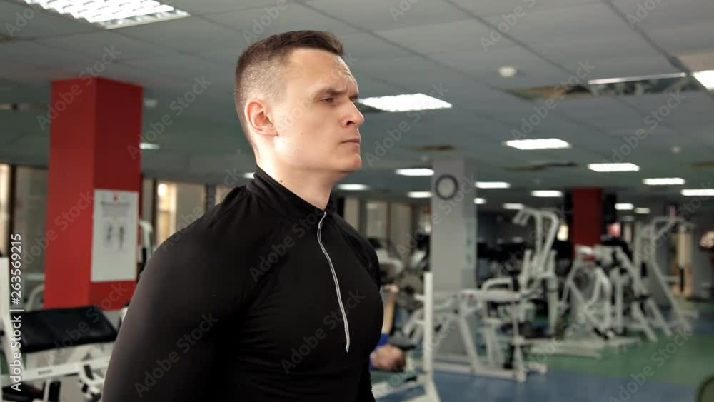 Young muscular built athlete working out in a gym, sitting on a weightlifting machine and lifting two dumbbells Young muscular built athlete working out in a gym, sitting on a weightlifting machine and lifting two dumbbells