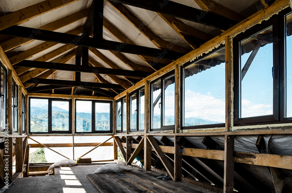 Fototapeta premium Building in the mountains: finishing work on the top floor of a private wooden house, a room with a panoramic view of the mountains.