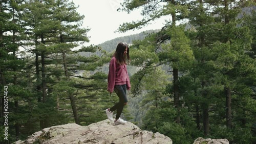 Teenage girl walking on rocks in the forest among pine trees