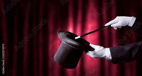 Fotografie magician hand holding a top hat and wand. high contrast image