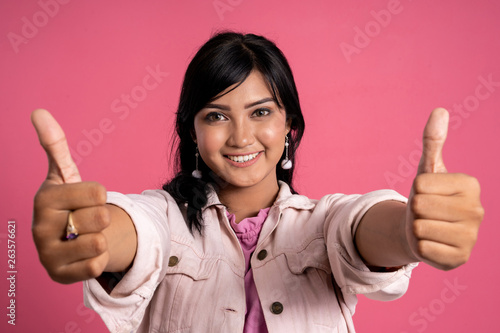 portrait of beautiful asian woman showing two thumbs up over pink background photo