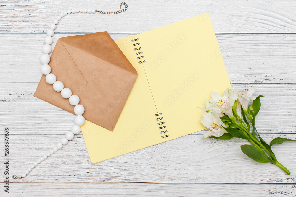 white lilies with yellow notebook and beads with craft envelope on white wooden table, top view, flat lay. white lilies with yellow notebook and beads with craft envelope on white wooden table, top view, flat lay.