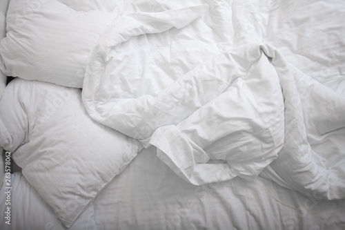 View on top of crumpled bed with white linens. Make the bed. Used dirty bedding. Fresh sheets. Crumpled sheets. Bed after sleeping in the morning. Pillow and blanket. Concept. Close up. Copy space.