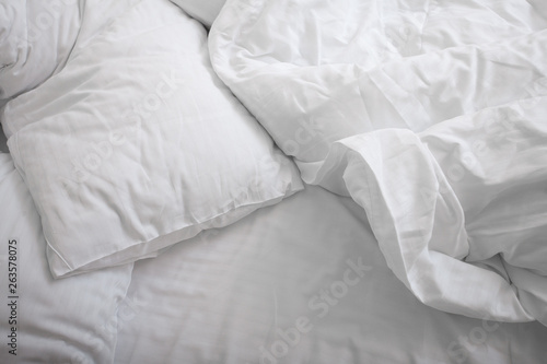 View on top of crumpled bed with white linens. Make the bed. Used dirty bedding. Fresh sheets. Crumpled sheets. Bed after sleeping in the morning. Pillow and blanket. Concept. Close up. Copy space.