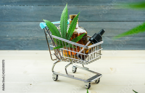 Supermarket trolley with marijuana leafs and medical cannabis oil cbd on wooden backdrop