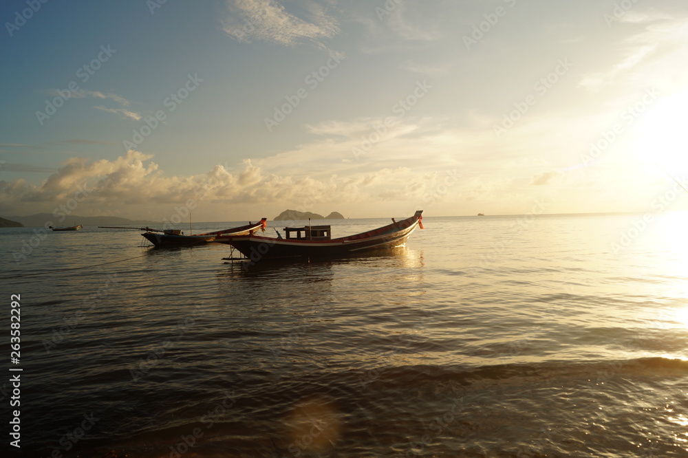 A beautiful sunset at the beach of Koh Phangan with boats and a bright sun, in Thailand