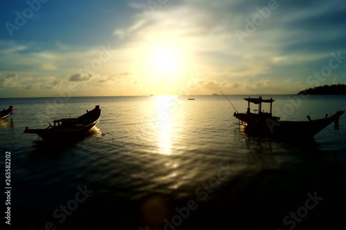 A beautiful sunset at the beach of Koh Phangan with boats and a bright sun, in Thailand