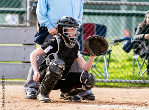 Female softball catcher in full protective gear ready to catch the first pitch.